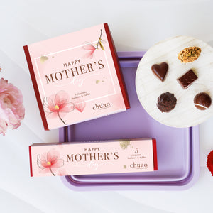 a red box containing chocolate bonbons on a plate inside with a mother's day theme of flowers and a purple dish
