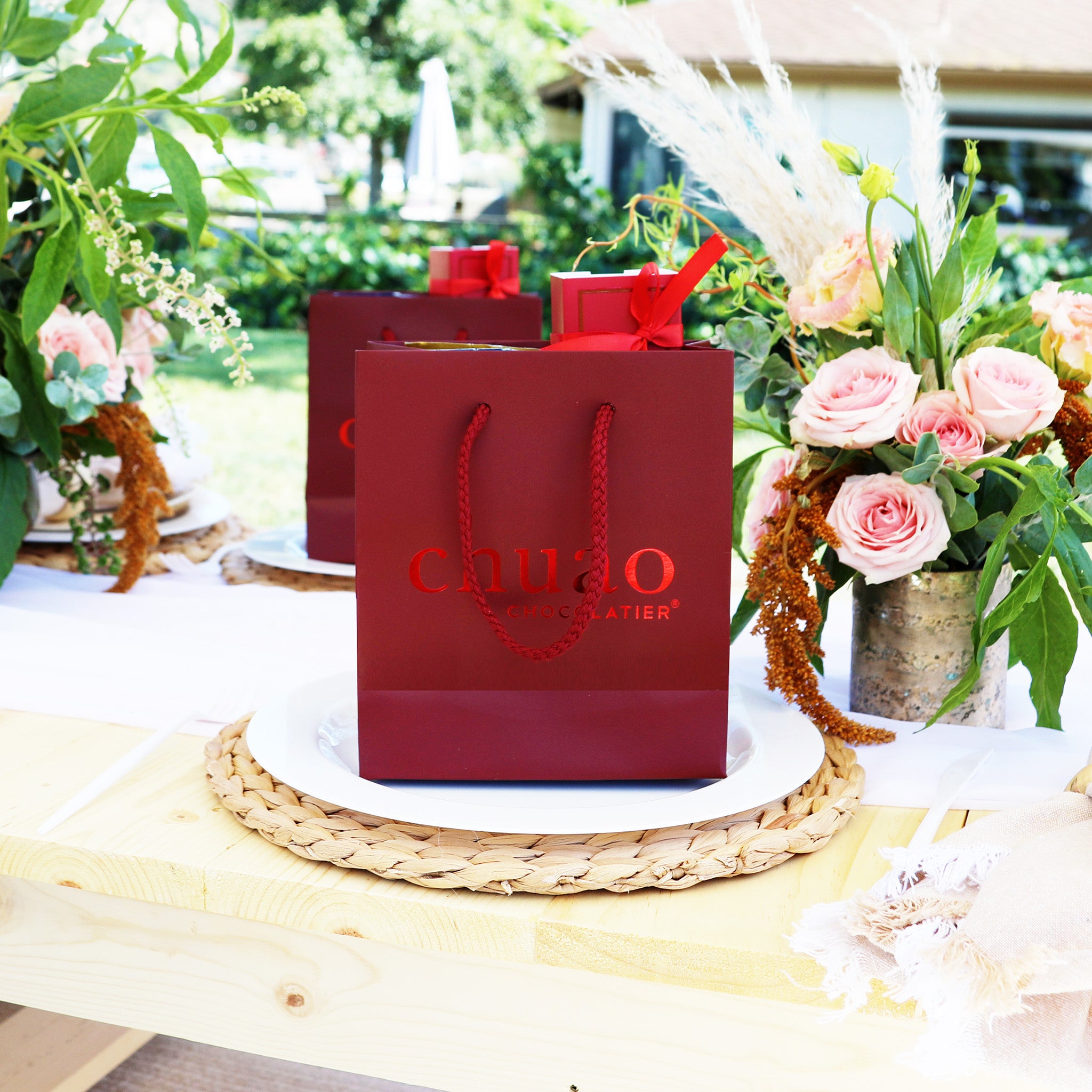 a chuao red gift bag on a place setting with bright flower arrangements