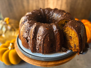 a Chocolate and pumpkin cake with a slice being pulled away in front of a backdrop of pumpkins