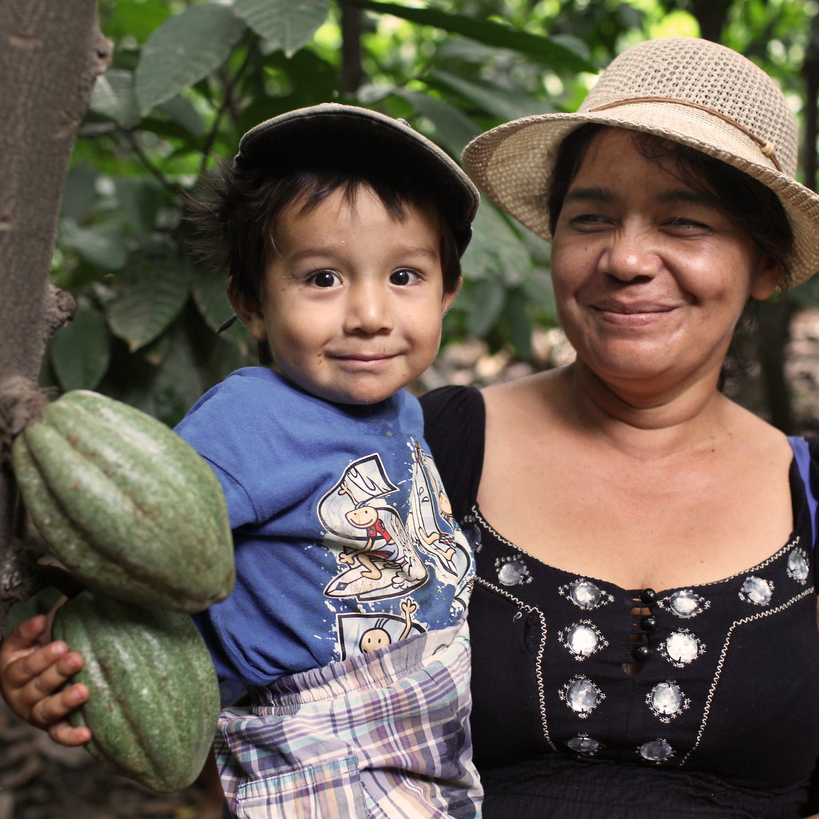 a smiling boy and mother holding cocoa beans in the jungle