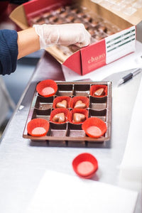Chocolate heart bonbons being placed in a tray with red wrapping