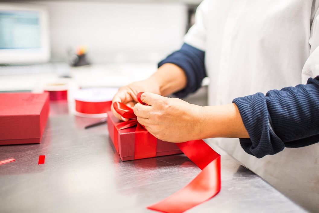 A worker wrapping a red chocolate gift box with a red bow